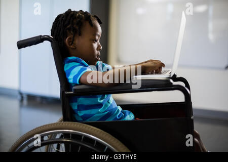 Disabled schoolboy on wheelchair using laptop Stock Photo