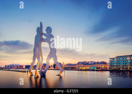 Germany, Berlin, Molecule Man Sculpture on Spree and illuminated riverfront at dusk