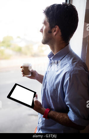 Profile view of businessman is holding a tablet and a coffee Stock Photo