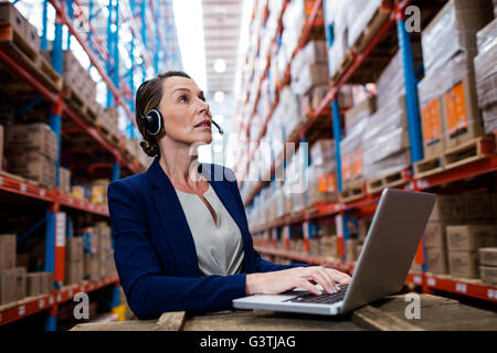 Warehouse manager looking up with her headset and laptop Stock Photo