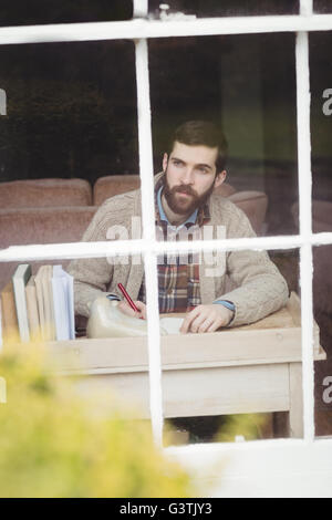 Handsome hipster man looking through window while writing Stock Photo
