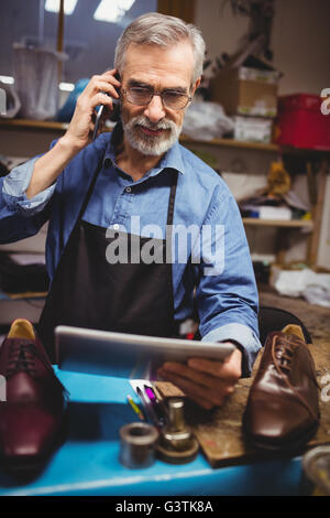 Portrait of cobbler calling with his mobile phone and holding a tablet computer Stock Photo