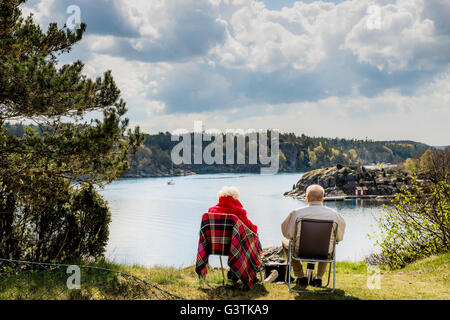 Sweden, West Coast, Bohuslan, Senior couple sitting on lounge chairs and looking at view