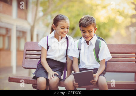 Happy school kids sitting on bench and using digital tablet Stock Photo