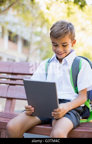 Schoolboy sitting on bench and using digital tablet in campus Stock Photo