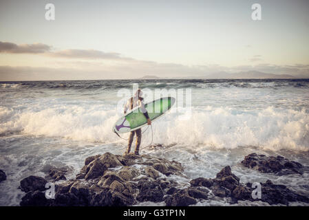 A man in a wetsuit preparing to surf at Corralejo in Fuerteventura. Stock Photo