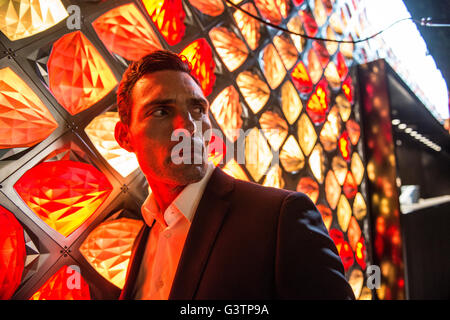 A smartly dressed man bathed in red light in front of a light fixture on the South Bank in London. Stock Photo