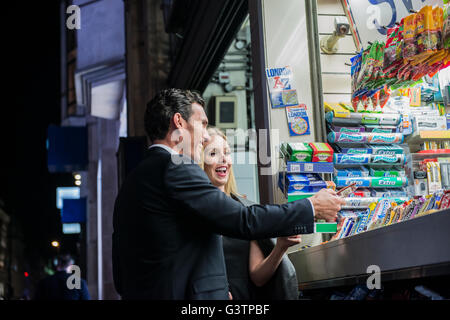 A smartly dressed couple buying confectionary from a kiosk on Oxford Street in London. Stock Photo