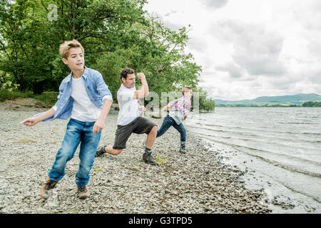A man and two boys skimming stones on the shore beside Bala Lake in Wales. Stock Photo