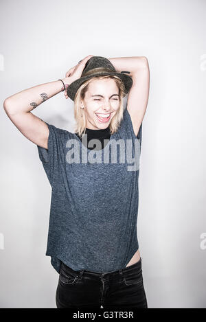 A young tattooed woman in a hat posing in a studio looking happy. Stock Photo