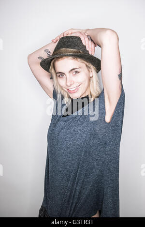 A young tattooed woman in a hat posing in a studio looking happy. Stock Photo