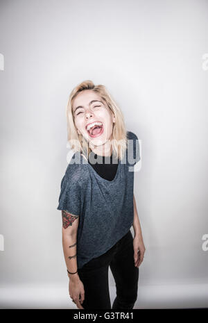 A young tattooed woman posing in a studio laughing. Stock Photo