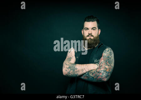 Studio portrait of a bearded man with tattooed arms. Stock Photo
