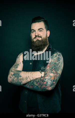 Studio portrait of a bearded man with tattooed arms. Stock Photo