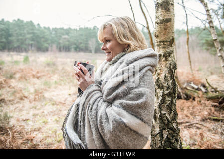 Senior lady standing wrapped in a blanket enjoying a cup of tea. Stock Photo
