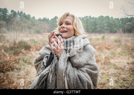 Senior lady standing wrapped in a blanket enjoying a cup of tea. Stock Photo