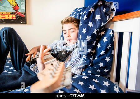 A ten year old boy laying on his bed playing a guitar. Stock Photo