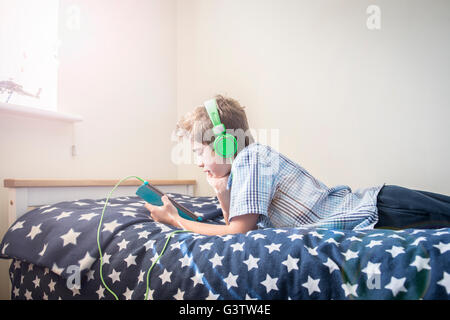 A ten year old boy laying on a bed listening to music on earphones. Stock Photo