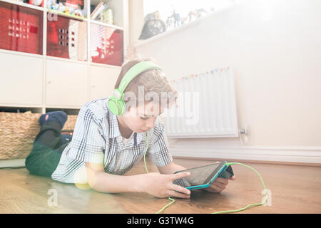 A ten year old boy laying on the floor listening to music on earphones. Stock Photo