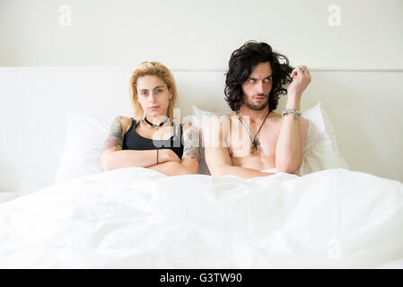 A cool young tattooed couple lying in a double bed after an arguement. Stock Photo