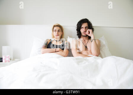 A cool young tattooed couple lying in a double bed after an arguement. Stock Photo