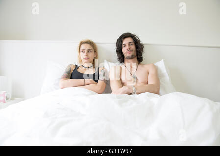 A cool young tattooed couple lying in a double bed after an arguement. Stock Photo