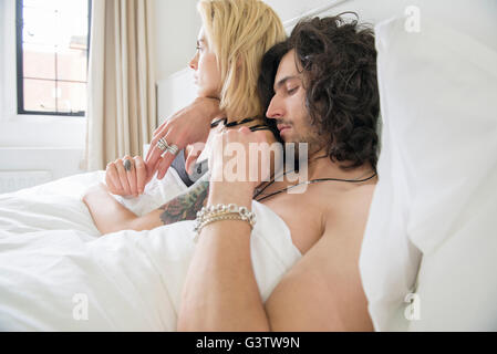 A cool young tattooed couple embracing in a bed. Stock Photo