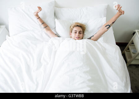 A cool young woman lying in a bed stretching her arms. Stock Photo