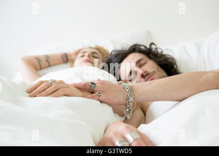 A cool young couple relaxing in bed with their eyes shut. Stock Photo