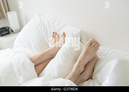 A couple lying in a bed with their feet sticking out from underneath the covers. Stock Photo