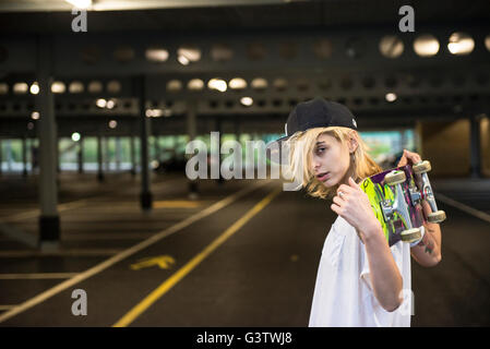A cool young tattooed skater girl carrying her skateboard over her shoulders. Stock Photo