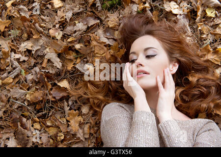An attractive young woman laying on the forest floor surrounded by leaves. Stock Photo