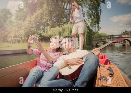 A couple with a guitar sitting in a punt on the River Cam in Cambridge. Stock Photo