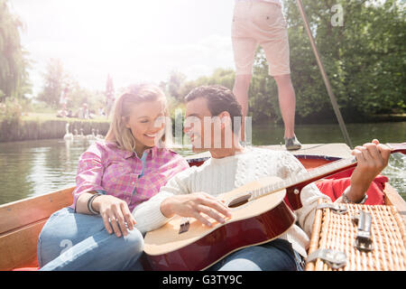 A couple with a guitar sitting in a punt on the River Cam in Cambridge. Stock Photo