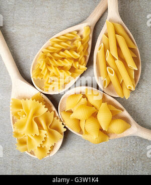 Various types of pasta in wooden spoons on stone table, top view Stock Photo