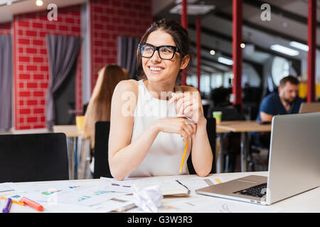 Portrait of smiling pretty young business woman in glasses sitting on workplace Stock Photo