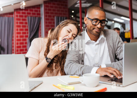 Tired bored young business people yawning and working with laptop in office Stock Photo