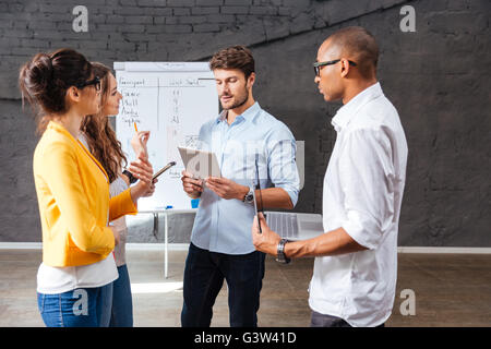 Group of confident young people standing and discussing new project in conference room Stock Photo