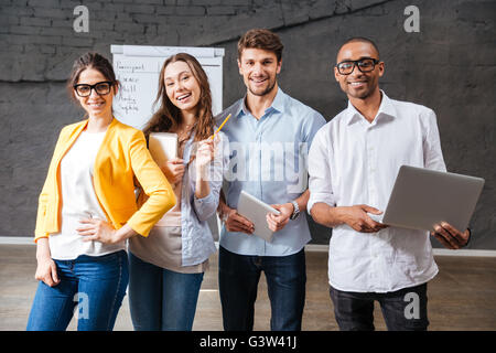Group of cheerful successful young business people with tablet and laptop standing in conference room Stock Photo