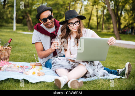 Smiling young couple listening to music and using laptop outdoors Stock Photo