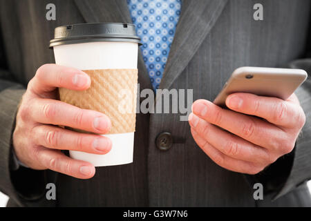 Businessman holding disposable cup of coffee and using smart phone Stock Photo