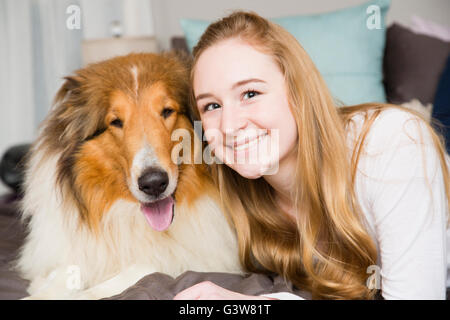 Portrait of teenage girl (14-15) and collie dog lying on bed Stock Photo