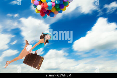 Young woman holding balloons and old suitcase, flying above clouds. Concept of travel and freedom Stock Photo