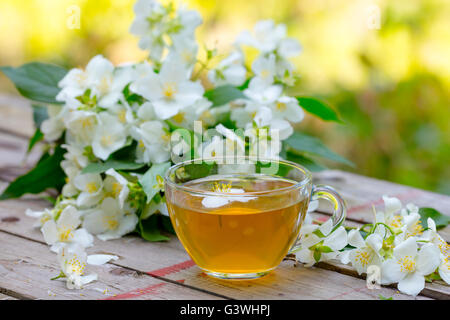 A cup of green tea with jasmine flowers on grunge wooden table outdoors Stock Photo