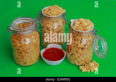 different sizes of pasta to choose from confined in glass jars with bowl of red sauce Stock Photo