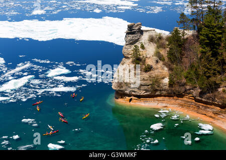 Kayaks maneuver through ice floes to view Miners Castle rock formation on Lake Superior. A late ice breakup Stock Photo