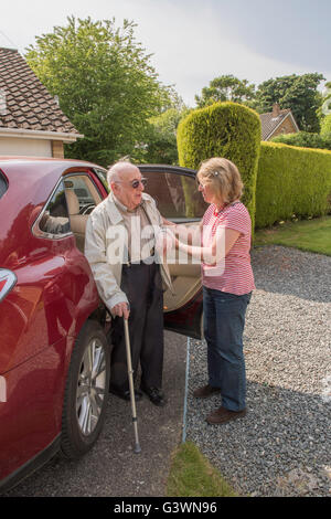 Man in his nineties arriving home in motor car, after possibly a hospital or doctors appointment, with daughter or carer. Stock Photo