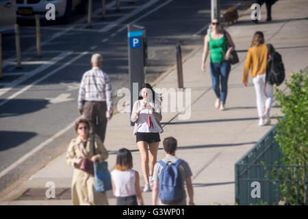 A woman walks down Ninth Avenue in the Chelsea neighborhood of New York distracted by her smartphone on Friday, June 10, 2016 . (© Richard B. Levine) Stock Photo