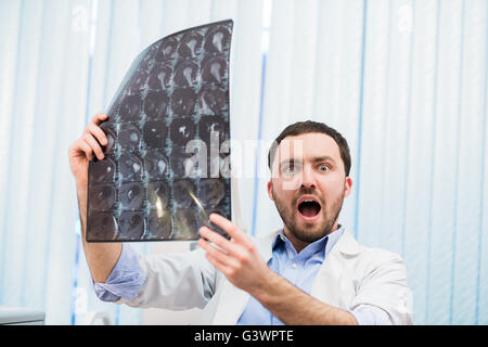 Scared worried doctor reviewing X-ray scan looking at the camera Indoors in office Stock Photo