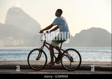 RIO DE JANEIRO - APRIL 3, 2016: Young Brazilian man rides a bicycle  on the beachfront boardwalk at Copacabana Beach. Stock Photo